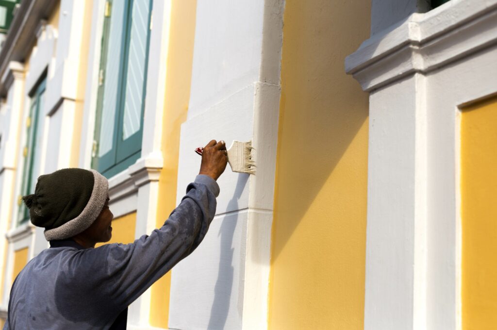 Professional house painter painting the exterior of a home yellow and white.