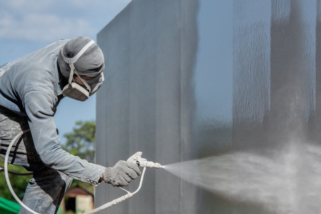 painting contractor using a sprayer and wearing protective gear