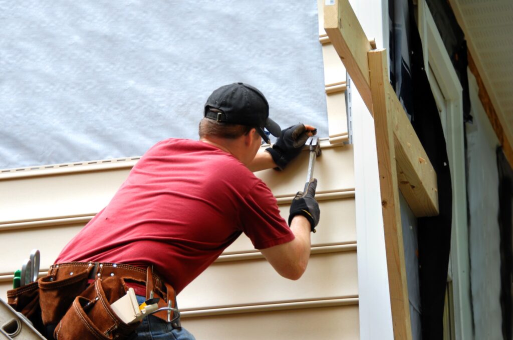 A man is repairing a home's siding to prepare for a professional exterior paint job.