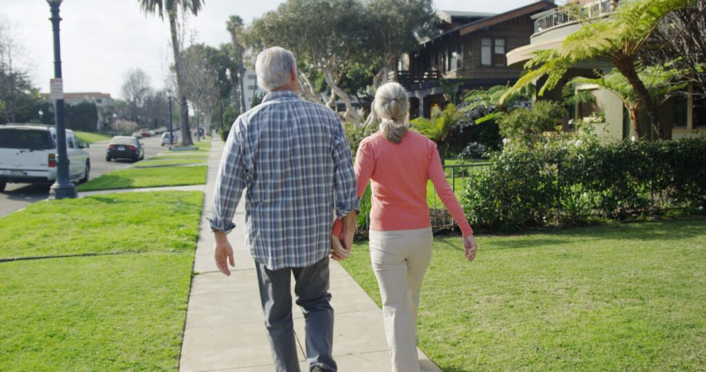 Keep your neighboring houses in mind when choosing home exterior paint colors. Image of older couple walking hand-in-hand in their neighborhood.