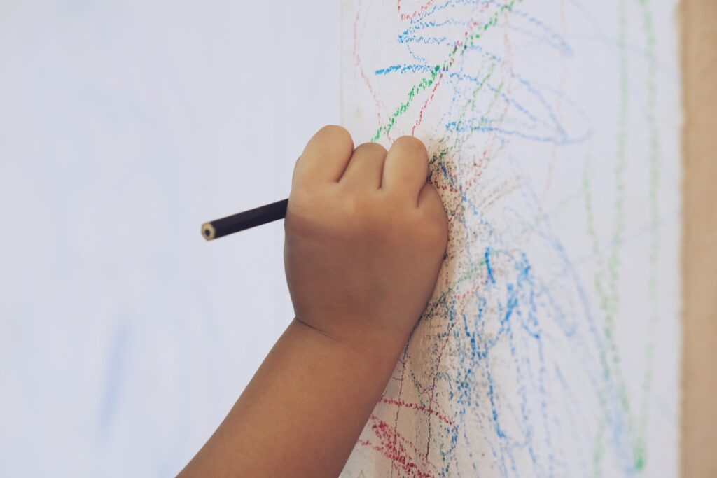Image of child's hand coloring on a white wall with pencils