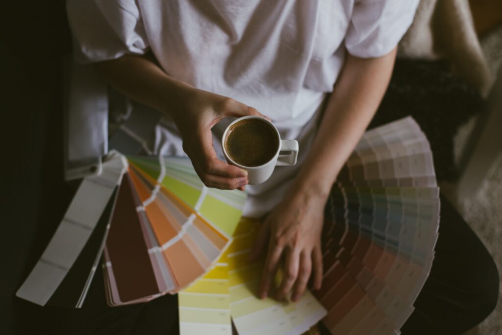 Image of woman holding a cup of coffee while looking at paint chip colors.