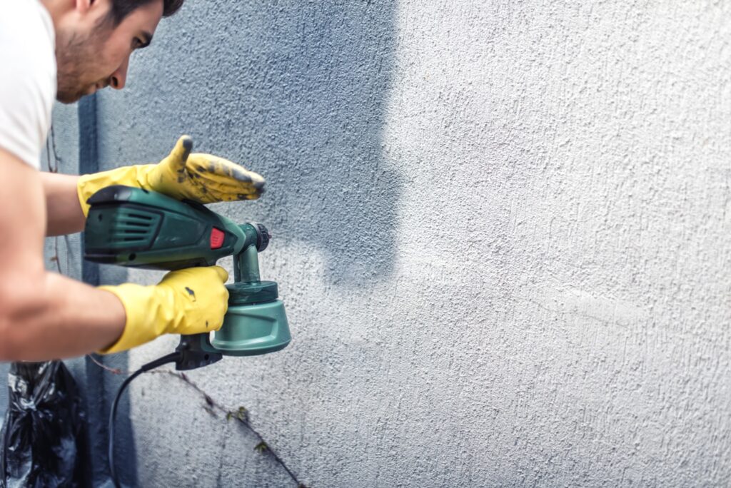 Image of professional painter spraying a home's exterior with gray paint.