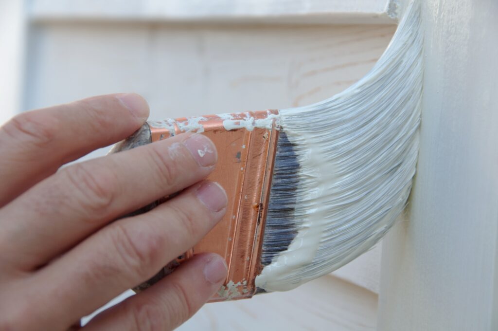 Closeup image of a a hand holding a paint brush to paint their home's exterior.